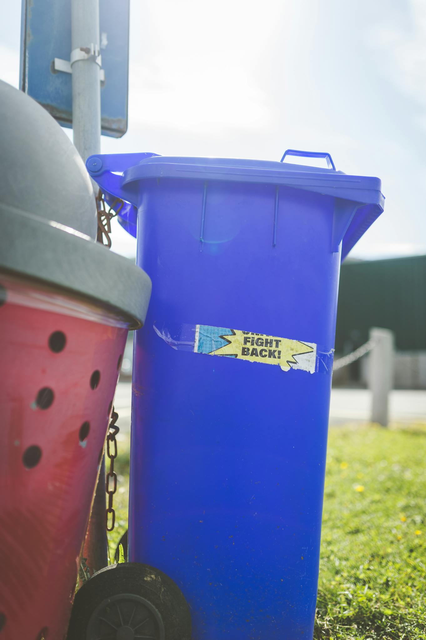 Bright blue trash bin with 'Fight Back!' label, outdoors on a sunny day.